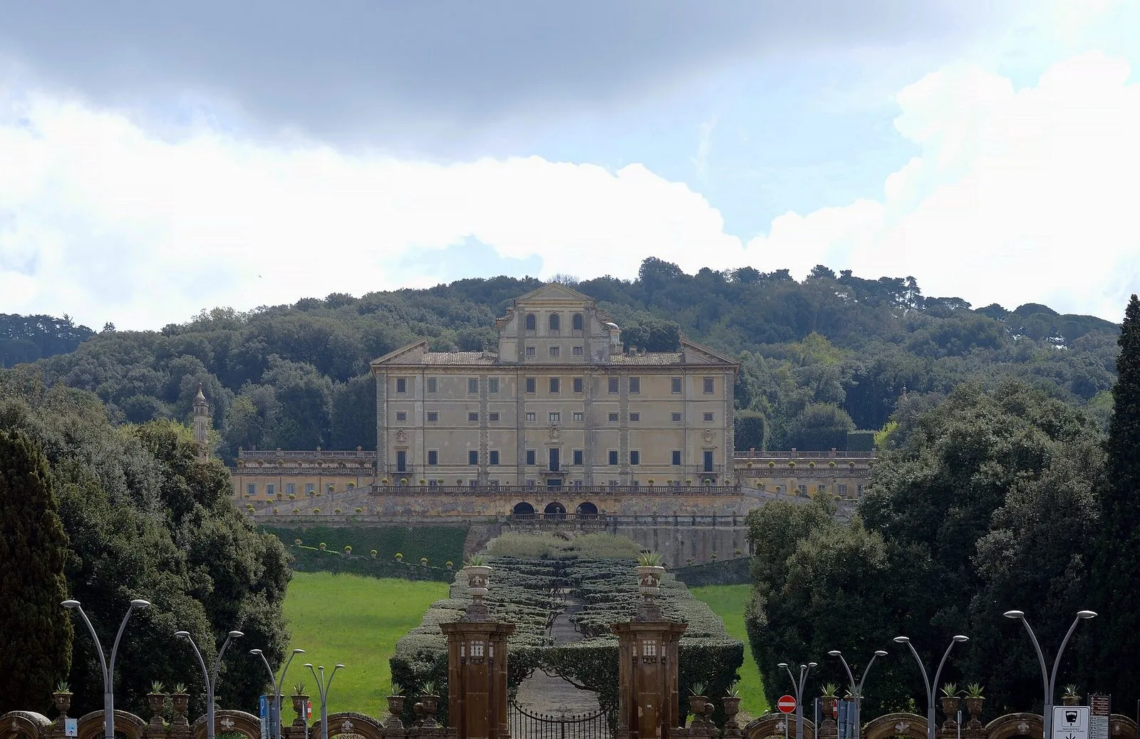 Facciata di Villa Aldobrandini a Frascati vista dal cancello d'ingresso, con il viale di siepi e il bosco alle spalle