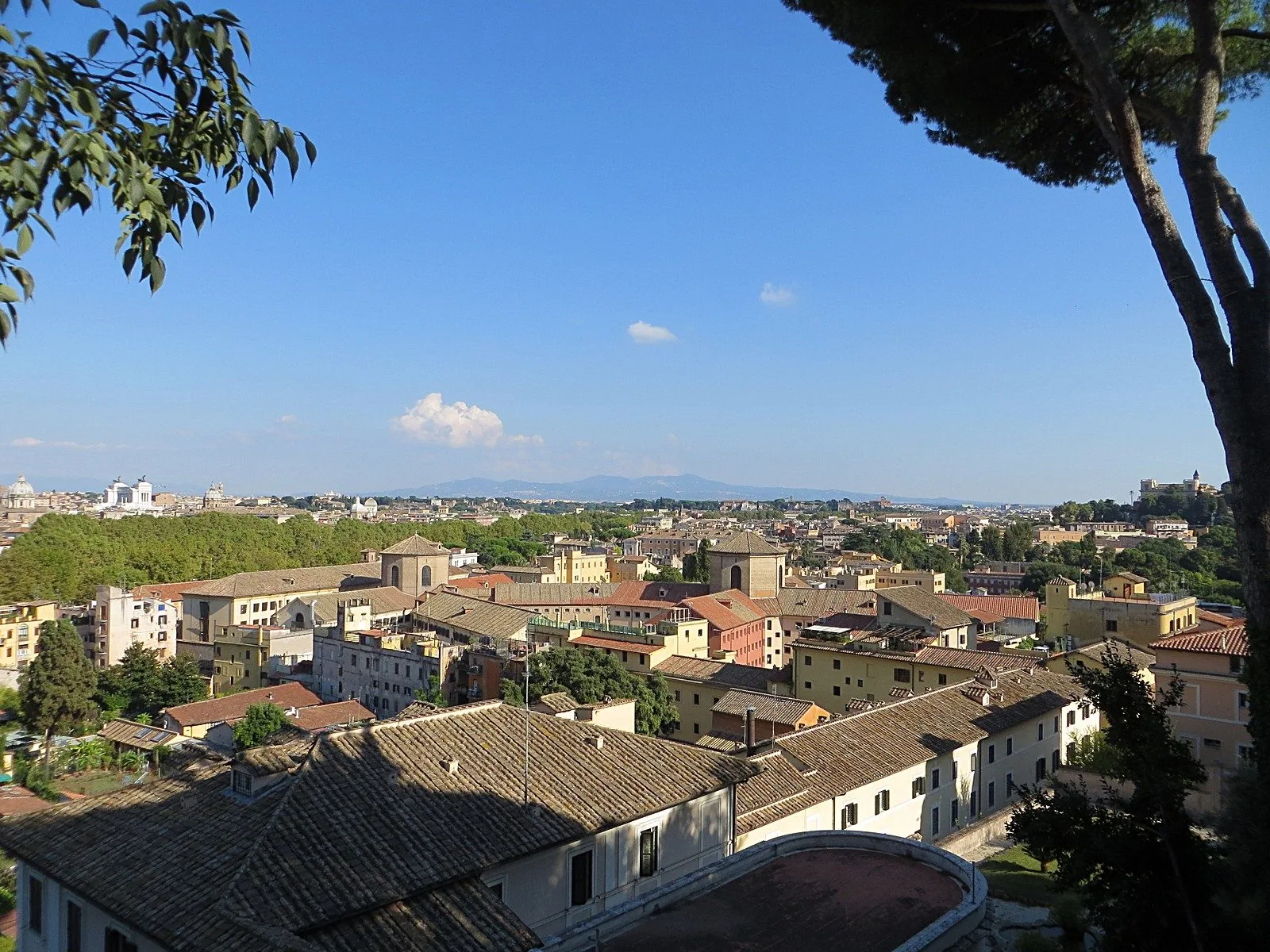 Panorama dei tetti di Roma sotto un cielo azzurro, con le colline sullo sfondo